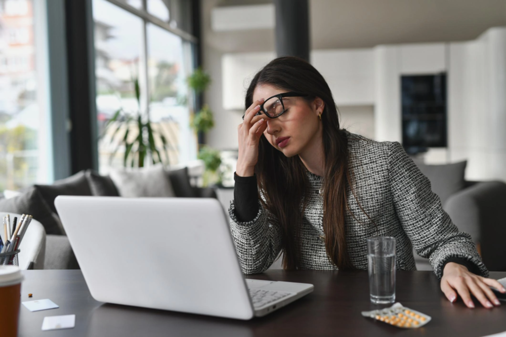 Stressed professional woman working on laptop holding her head showing signs of burnout and fatigue
